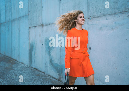 Happy young woman wearing red dress marcher le long street Banque D'Images