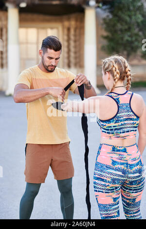 Entraîneur de boxe fitness pratique classe avec jeune femme à l'extérieur dans la ville de bandage application Banque D'Images