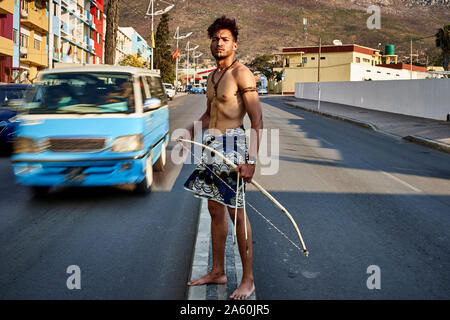 L'homme Tribal avec son arc et flèches traditionnelles au milieu de la ville avec des voitures qui passent, Lubango, Angola Banque D'Images