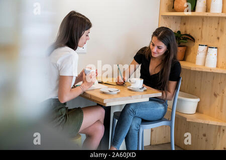 Deux jeunes femmes prenant des notes dans un café Banque D'Images