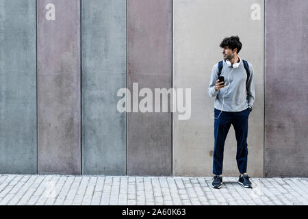 Man with cell phone et écouteurs debout devant des awall Banque D'Images