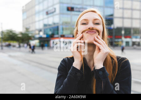 Portrait de jeune femme rousse faire moustache avec ses cheveux, Berlin, Allemagne Banque D'Images