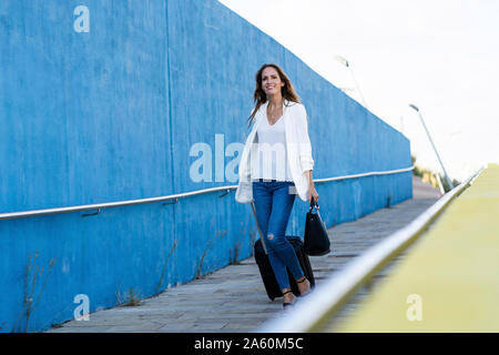 Businesswoman avec bagages à marcher le long du mur bleu Banque D'Images