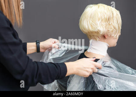 Coiffure est de mettre une feuille de plastique pour couvrir son client lors de la mort de cheveux. Cliente est en attente pour la teinture des cheveux. Banque D'Images