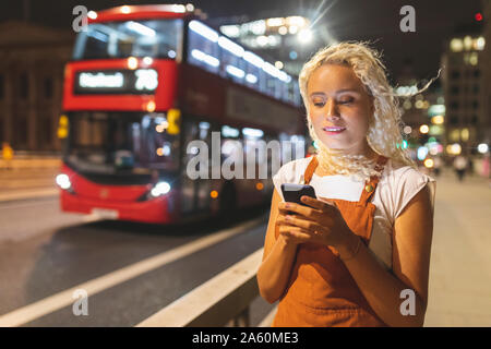 Jeune femme à Londres la nuit à la recherche de son smartphone Banque D'Images