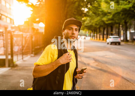 Portrait de jeune homme à l'écoute de la musique avec des écouteurs et en bordure d'attente smartphone Banque D'Images