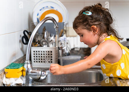 Petite fille lave-vaisselle dans le robinet de cuisine à la maison Banque D'Images