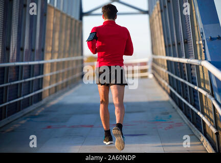Vue arrière d'un jogger avec le smartphone dans la poche du bras tournant sur un pont Banque D'Images