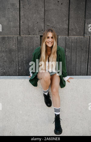 Portrait of smiling woman wearing green jacket assis sur un mur, Vienne, Autriche Banque D'Images