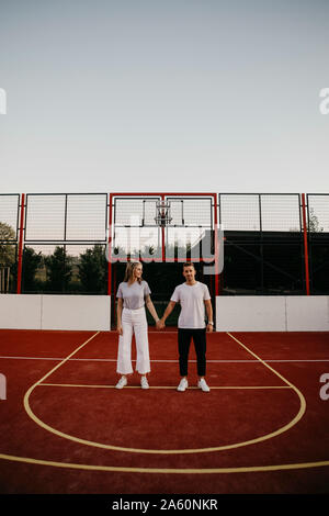 Jeune couple sur un terrain de basket-ball, holding hands Banque D'Images