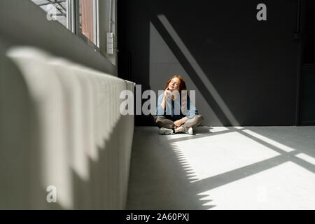 Redheaded woman sitting on floor of a loft bénéficiant du soleil Banque D'Images