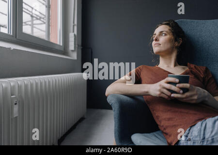 Jeune femme avec tasse de café on lounge chair à la fenêtre de Banque D'Images