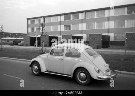 Modifier Käfer auf einer vor Neubauwohnungen Straße, Niederlande 1971. Une vieille Beetle conduire sur la route en face de nouveaux boîtiers, Pays-Bas 1971. Banque D'Images