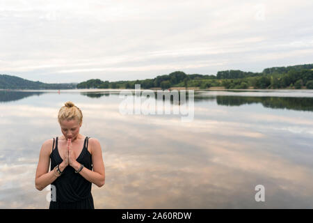 Jeune femme aux mains jointes à un lac Banque D'Images