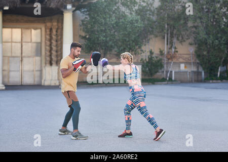 Entraîneur de boxe fitness pratique classe avec jeune femme à l'extérieur dans la ville Banque D'Images