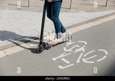 Les jambes de l'homme monté sur l'e-scooter sur piste cyclable dans la ville Banque D'Images