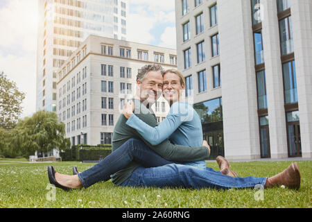 Couple assis sur le gazon dans la ville Banque D'Images