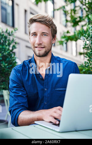 Portrait of young businessman with laptop à un café en plein air dans la ville Banque D'Images