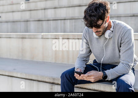 Homme assis sur un escalier extérieur using smartphone Banque D'Images