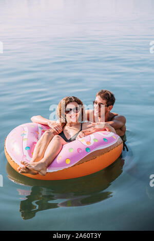 Happy young couple baignade en mer sur flotteur gonflable en forme de beigne Banque D'Images