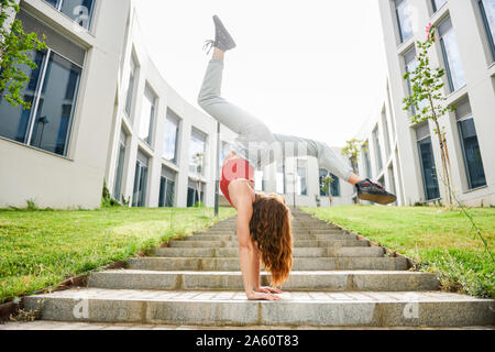 Young woman doing handstand sur un escalier extérieur Banque D'Images