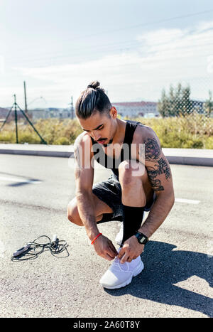 Jeune homme sportif chaussures de liage avant l'entraînement sur une route Banque D'Images