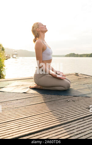 Young woman practicing yoga sur une jetée au bord d'un lac Banque D'Images