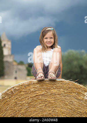 Portrait of smiling little girl sitting on hay bale Banque D'Images