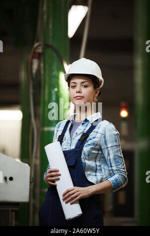 Portrait of female engineer en salopette et au travail de casque tout en se tenant dans l'usine Banque D'Images