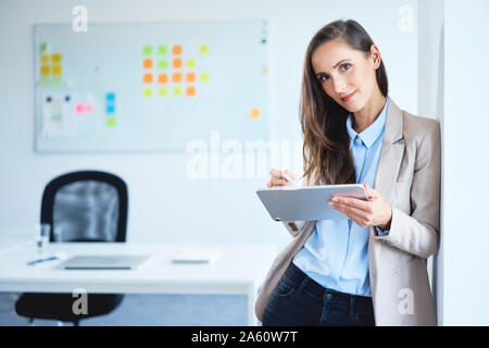 Young businesswoman smiling at camera while using tablet in office Banque D'Images