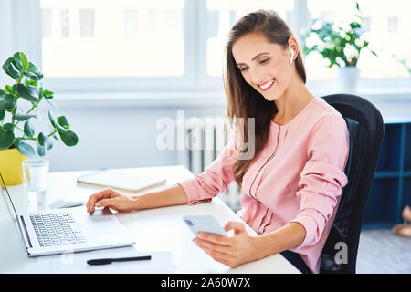 Young businesswoman phone alors que working on laptop in office Banque D'Images
