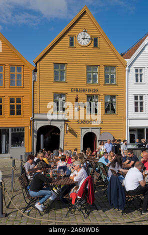 Les touristes s'asseoir au soleil dans les bars et cafés en plein air dans le vieux quai et bâtiments traditionnels en bois dans le quartier de Bryggen, Bergen, Norvège Banque D'Images