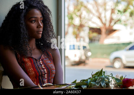 Portrait de jeune femme africaine avec des fleurs sur la table dans un café, à la fenêtre de Banque D'Images