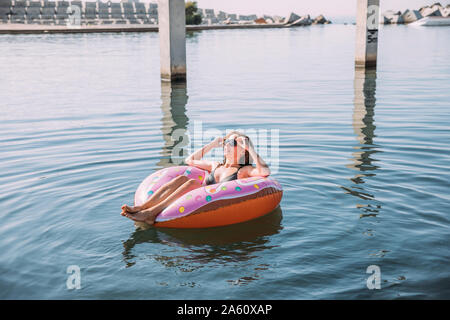 Jeune femme se baignant dans la mer sur flotteur gonflable en forme de beigne Banque D'Images