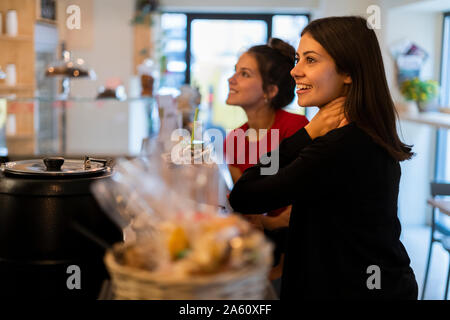 Deux jeunes femmes souriant au comptoir d'un café Banque D'Images