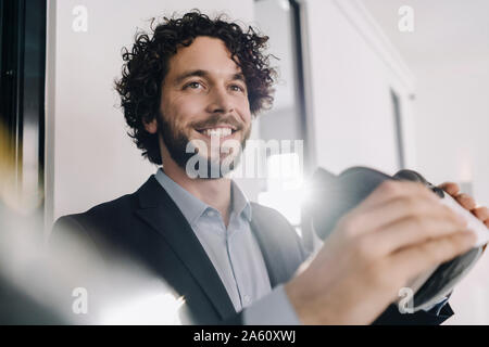 Portrait of smiling businessman holding lunettes VR in office Banque D'Images