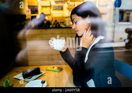 Jeune femme dans un café derrière la vitre Banque D'Images