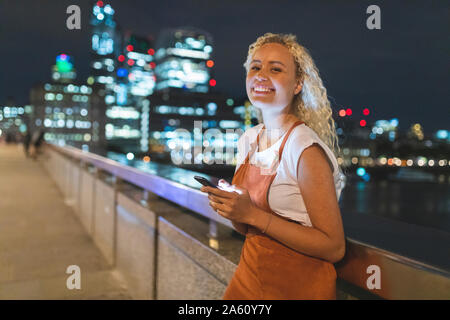 Jeune femme à Londres la nuit à l'aide de son smartphone Banque D'Images