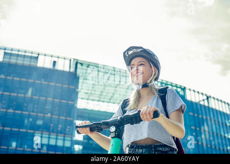 Portrait of smiling young woman with E-scooter dans la ville, Berlin, Allemagne Banque D'Images
