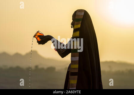 Woman in traditional Ahir chiffon coloré verser de l'eau au coucher du soleil, le grand désert du Rann de Kutch, Gujarat, Inde, Asie Banque D'Images