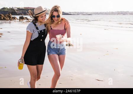 Deux copines s'amuser, marcher sur la plage, en tenant vos autoportraits smartphone Banque D'Images