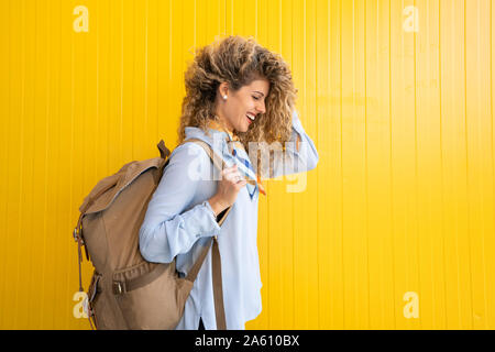 Laughing young woman carrying backpack en face de fond jaune Banque D'Images