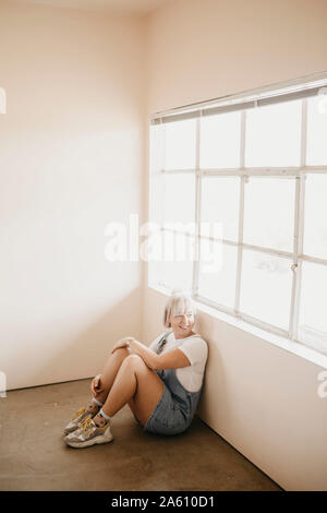 Souriante jeune femme assis sur le plancher d'une chambre Banque D'Images