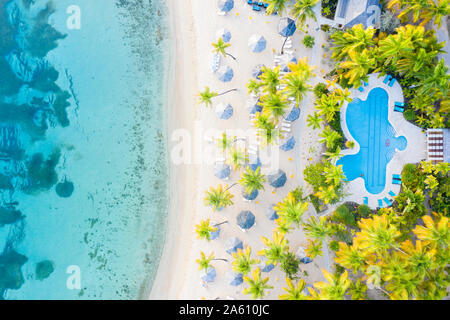 Une piscine extérieure et des parasols sur la plage de sable blanc du dessus par drone, Morris Bay, Old Road, Antigua, Iles sous le vent, Antilles, Caraïbes Banque D'Images