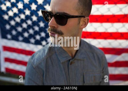 Jeune homme avec des lunettes de soleil en face de nous-drapeau américain sur fence Banque D'Images