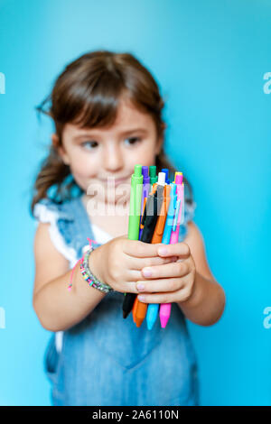 Portrait of cute little girl picking up une poignée de stylos à bille de couleur sur fond bleu Banque D'Images