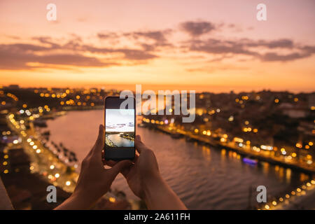 Woman's hands holding smartphone avec une photo d'une vue panoramique sur Porto, Portugal, au coucher du soleil Banque D'Images