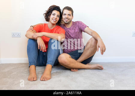 Portrait of happy couple assis sur le plancher à new home Banque D'Images