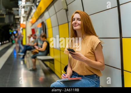 Femme à l'aide de la station de métro de smartphone Banque D'Images