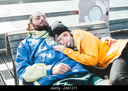 Couple lying aux yeux clos sur un banc en bois à la plage Banque D'Images